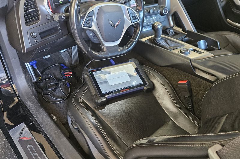Inside a Corvette with the door open and a programming tablet on the seat, being worked on where it was parked.