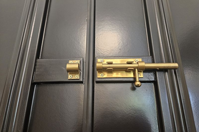 A brass slide bolt newly fitted to a dark-painted wooden door.